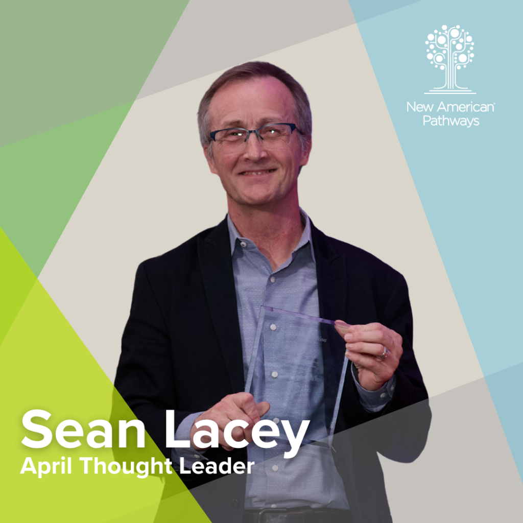 Portrait of Sean Lacey, April Thought Leader for New American Pathways, smiling and holding a clear award plaque against a geometric green and blue background with the organization’s logo.