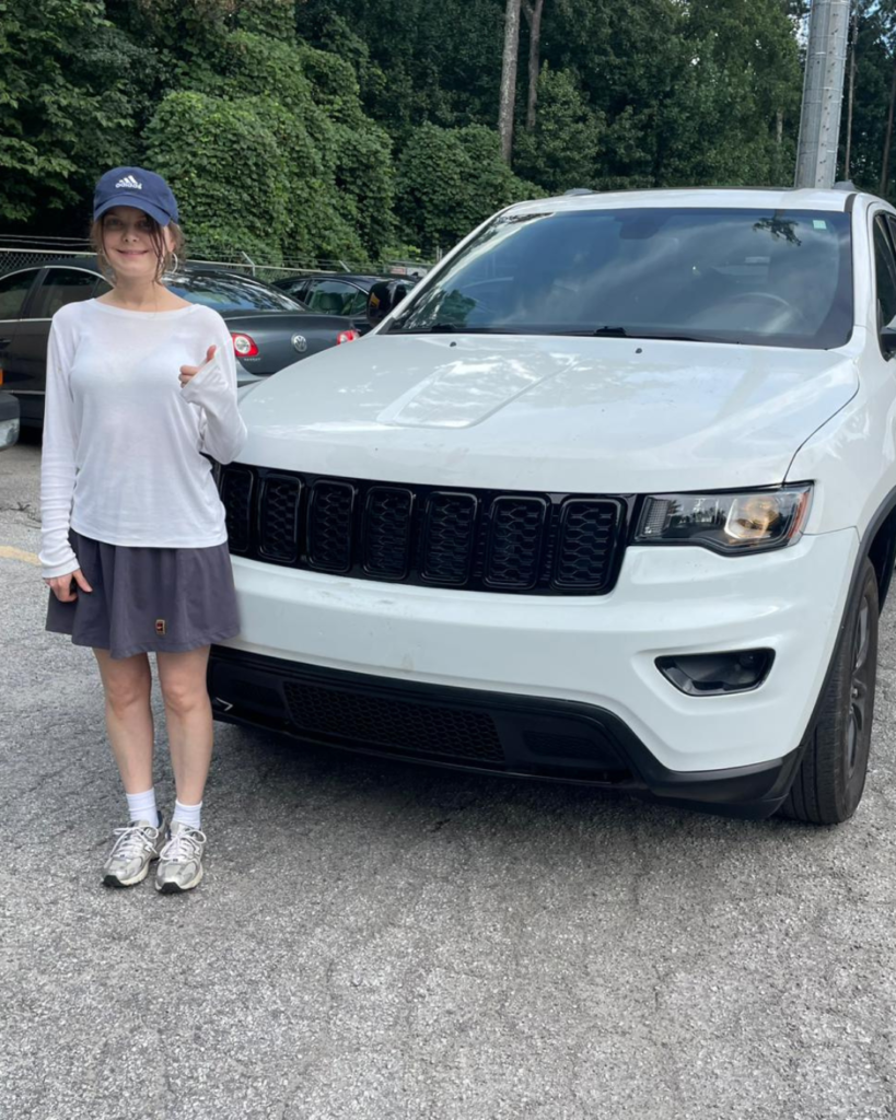 New American Pathways client stands beside a white SUV, celebrating the purchase of a vehicle and a step toward greater independence.